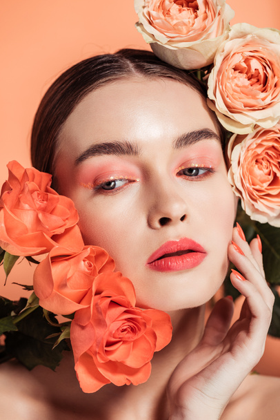 beautiful stylish girl touching face and posing with rose flowers isolated on coral - Φωτογραφία, εικόνα