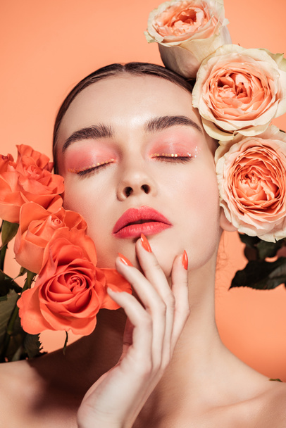 beautiful stylish girl touching face and posing with rose flowers isolated on coral - Foto, afbeelding