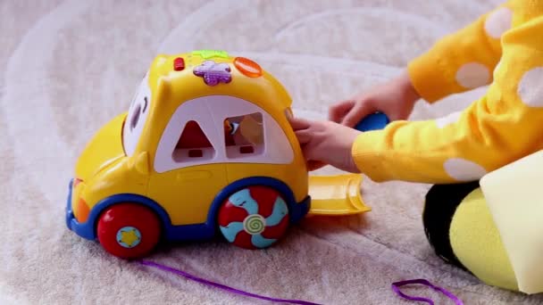 Niña juega con coche de juguete educativo amarillo, sentado en un piso en el jardín de infantes
 . - Metraje, vídeo