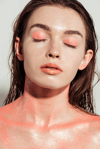 hermosa chica con maquillaje de brillo de coral y los ojos cerrados posando aislado en gris
 - Foto, Imagen