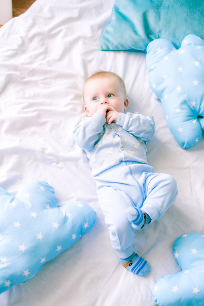 Cute toddler boy on bed at home surrounded by blue pillows - Foto, afbeelding