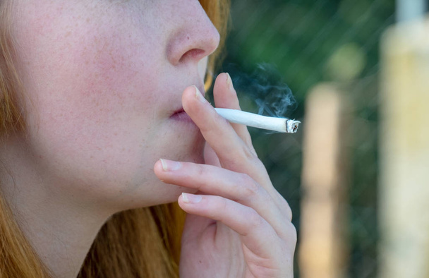 Χέρι και το στόμα στο προφίλ και χέρι-έλασης τσιγάρο από μια εθισμένη νεαρή γυναίκα τραβώντας σκληρά σε ένα τσιγάρο, με χώρο για το κείμενό σας, αντιγραφή χώρου - Φωτογραφία, εικόνα