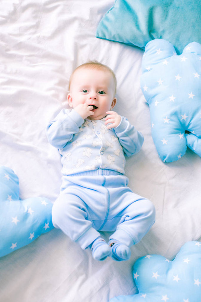 Cute toddler boy on bed at home surrounded by blue pillows - Фото, зображення