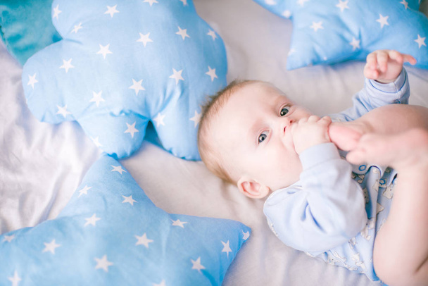 Cute toddler boy on bed at home surrounded by blue pillows - Zdjęcie, obraz