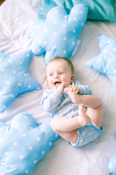 Cute toddler boy on bed at home surrounded by blue pillows - Фото, зображення
