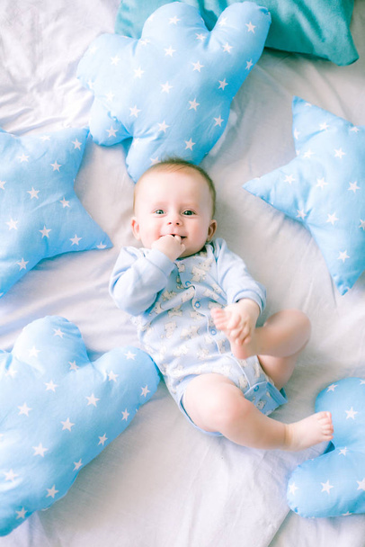 Cute toddler boy on bed at home surrounded by blue pillows - Photo, Image