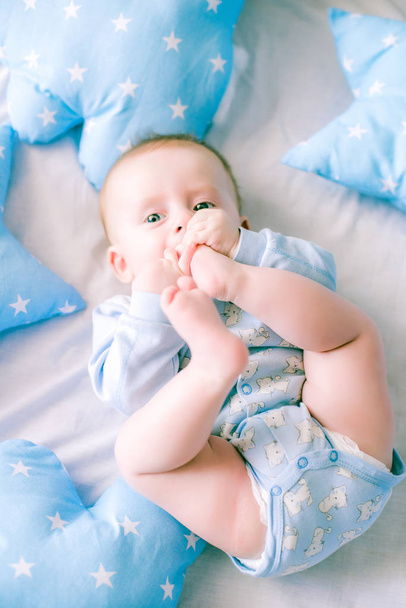 Cute toddler boy on bed at home surrounded by blue pillows - Foto, Bild