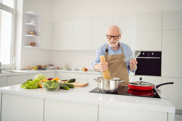 Close up photo excited grey haired he his him grandpa frying boiling uncooked pasta busy delicious dish process enjoy favorite stuff wear specs casual checkered plaid shirt jeans denim outfit kitchen - 写真・画像