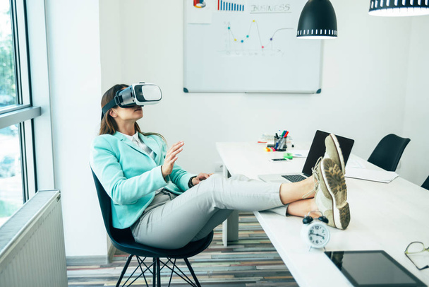 Молодая деловая женщина в наушниках VR, сидя в офисе
 - Фото, изображение