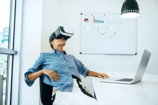 Young businesswoman wearing VR headset while sitting in office - Fotografie, Obrázek