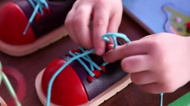 Маленькая девочка учится завязывать шнурки на игрушечных туфлях
. - Кадры, видео