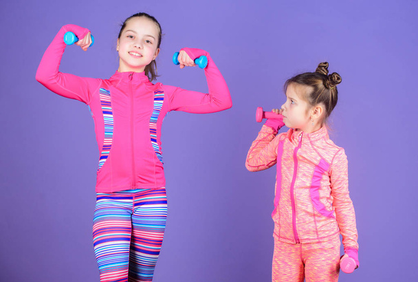 Motivation and sport example concept. Toddler repeat exercise after sister. Sport exercises for kids. Healthy upbringing. Sporty babies. Following her sister. Girls cute kid exercising with dumbbells - Photo, Image