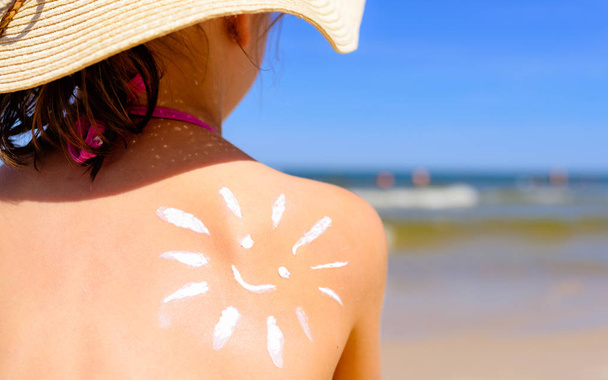 Meisje met zonnecrème op het strand in de vorm van de zon - Foto, afbeelding