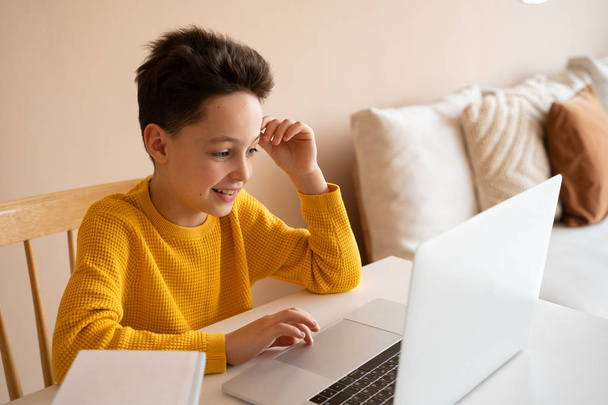 Cute little boy using laptop while doing homework in light room - Foto, afbeelding