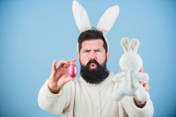 Calm down and celebrate. Hipster with long rabbit ears holding egg laying hare. Bearded man with bunny toy and Easter egg. Easter bunny delivering colored eggs. Celebration of spring time holiday - Zdjęcie, obraz
