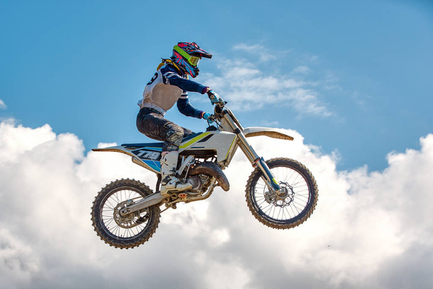 Extrém sportok háttér - sziluettje motoros Ugrás a motorkerékpárral a naplemente, szemben a kék ég, a felhők - Fotó, kép