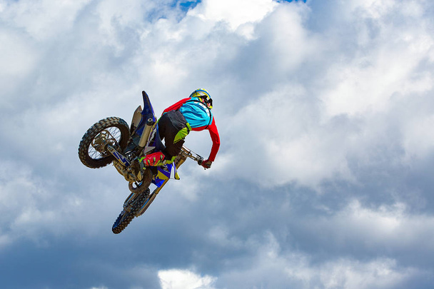 Fondo de deportes extremos - silueta de motociclista saltando en moto al atardecer, contra el cielo azul con nubes
 - Foto, Imagen