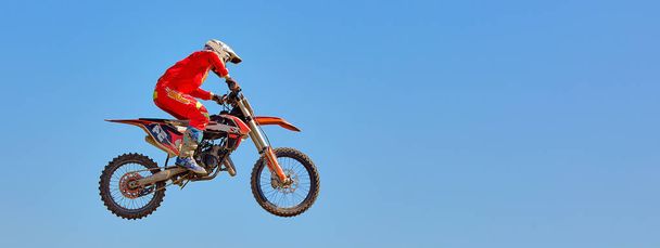 На спортивном фоне - силуэт байкера, прыгающего на мотоцикле на закате, на фоне голубого неба
 - Фото, изображение