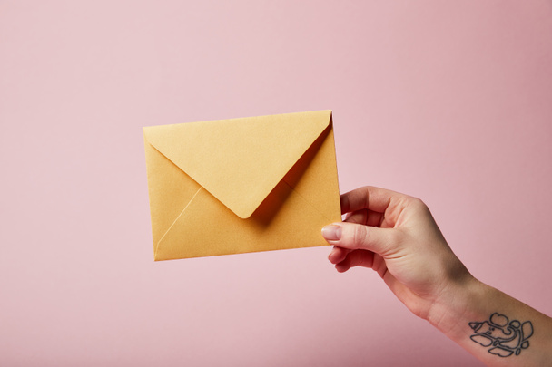 partial view of woman with tattoo holding yellow envelope on pink background  - Photo, Image