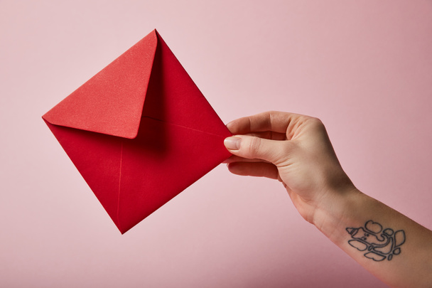 partial view of woman with tattoo holding red envelope on pink background  - Photo, Image