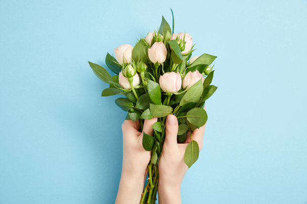 partial view of female hands with beautiful bouquet of roses on blue  - Photo, image