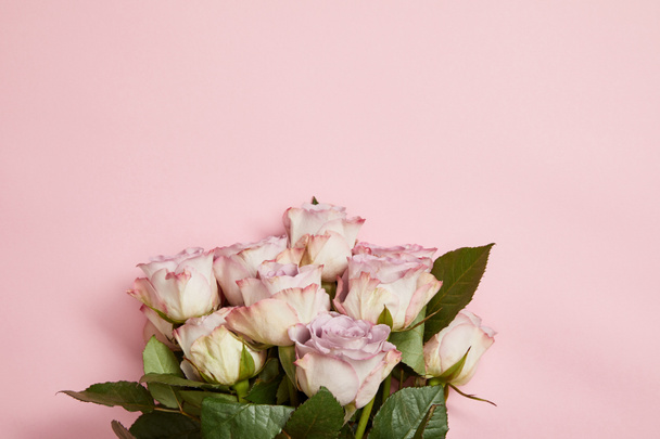 top view of beautiful bouquet of pink roses with green leaves on pink background - Foto, immagini