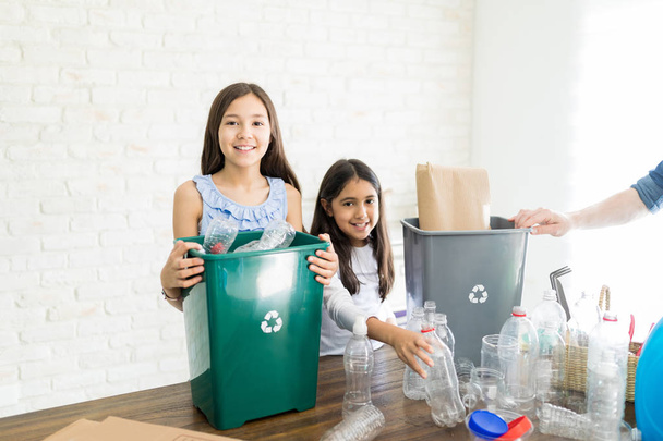 Lachende eco-vriendelijke broers en zussen met plastic afval thuis - Foto, afbeelding
