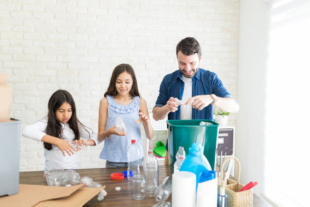 Father teaching daughters to crush the empty mineral water bottles before throwing them out - 写真・画像
