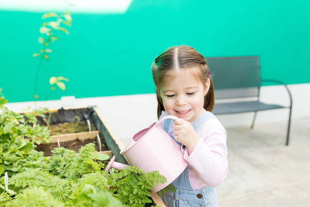 Niña preescolar aprendiendo a regar plantas mientras está de pie en el patio trasero
 - Foto, imagen