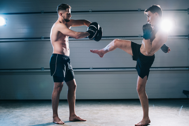 strong muscular shirtless mma fighter practicing high kick with another sportsman  - Photo, Image