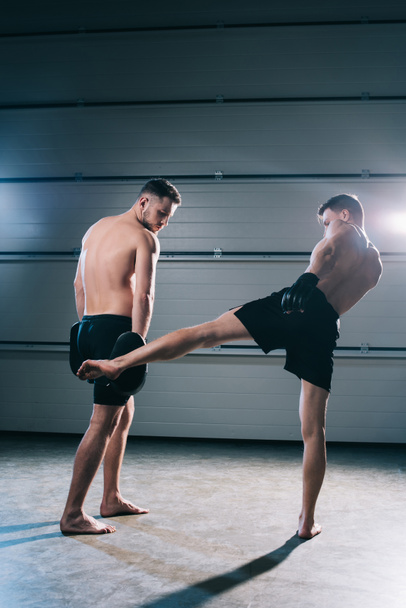 strong muscular shirtless mma fighter practicing low kick with another sportsman  - Photo, Image