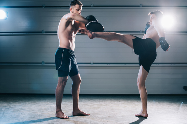 сильный мускулистый боец Мма практикующий высокий удар с другим спортсменом во время тренировки
 - Фото, изображение