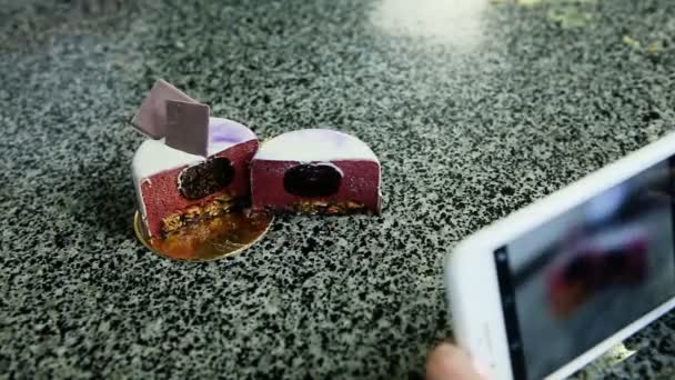 take photo on phone of cut in half purple glazed mousse mini cake with berry jam filling served on kitchen table - Footage, Video