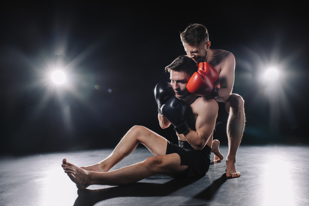strong mma fighter in boxing gloves doing painful chokehold to another sportsman on floor - Photo, Image