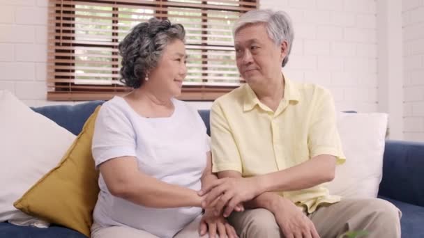 Casal de idosos asiáticos segurando as mãos enquanto tomam juntos na sala de estar, casal se sentindo feliz compartilhar e apoiar uns aos outros deitado no sofá em casa. Estilo de vida Família sênior em casa conceito
. - Filmagem, Vídeo