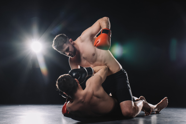 paidaton vahva mma taistelija nyrkkeilyhanskat lyömällä vastustaja päähän, kun urheilija makaa lattialla
 - Valokuva, kuva
