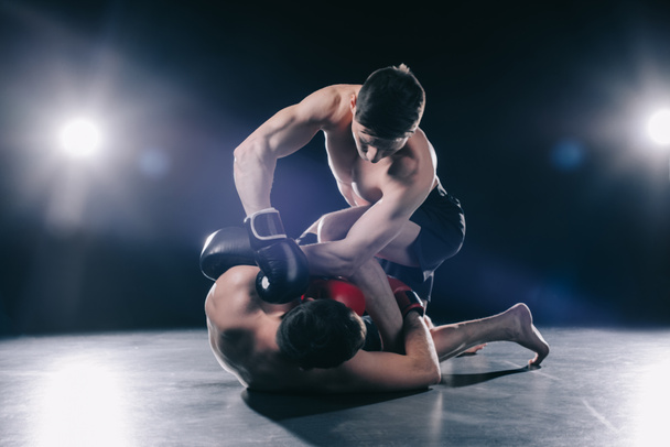 без рубашки мускулистый сильный боец Мма в боксёрских перчатках клинч оппонент на полу
 - Фото, изображение