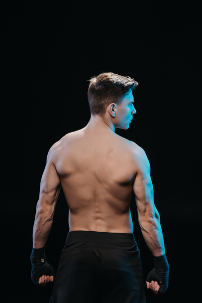 back view of muscular sportsman in bandages and blue light isolated on black - Fotografie, Obrázek