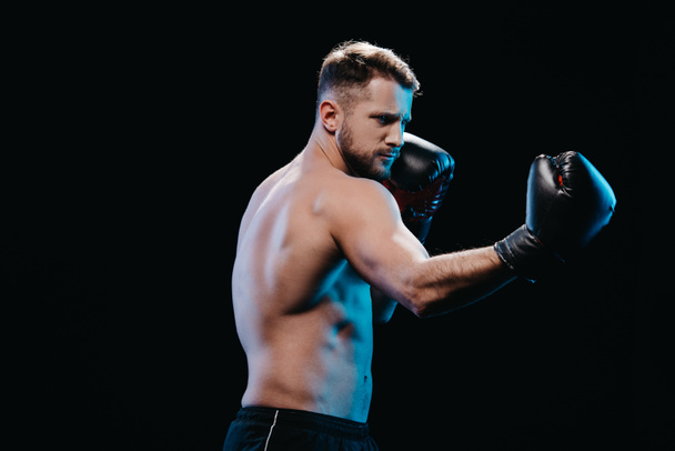 muscular shirtless strenuous boxer in boxing gloves doing punch isolated on black - Φωτογραφία, εικόνα