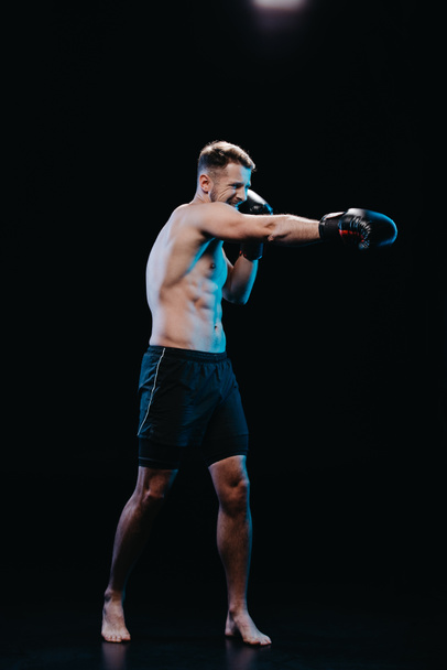 mezítláb sportos boxer megerőltető arc kifejezése a boksz-kesztyűket csinál ütés elszigetelt fekete - Fotó, kép