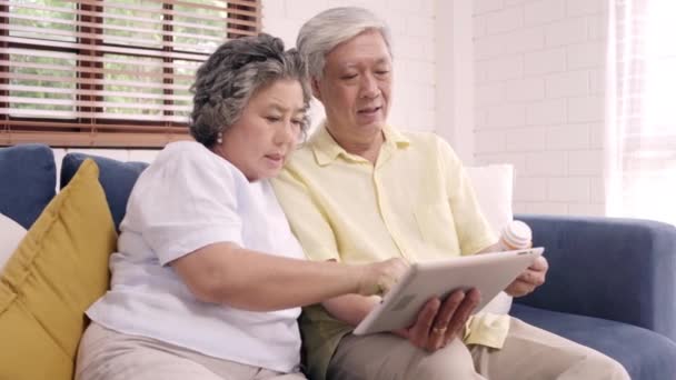 Asian elderly couple using tablet search medicine information in living room, couple using time together while lying on sofa when relaxed at home. Senior family health at home concept. - Video