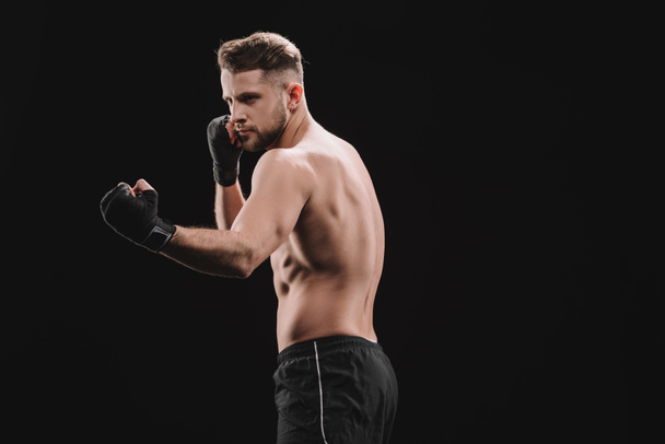 strong muscular mma fighter in bandages doing punch isolated on black - Photo, Image