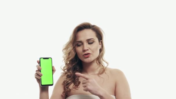 Distressed woman points finger at green screen of smartphone - Imágenes, Vídeo