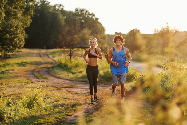 Happy Caucasian couple in sportswear with healthy habits running in nature. Sunny summer day. - Photo, Image