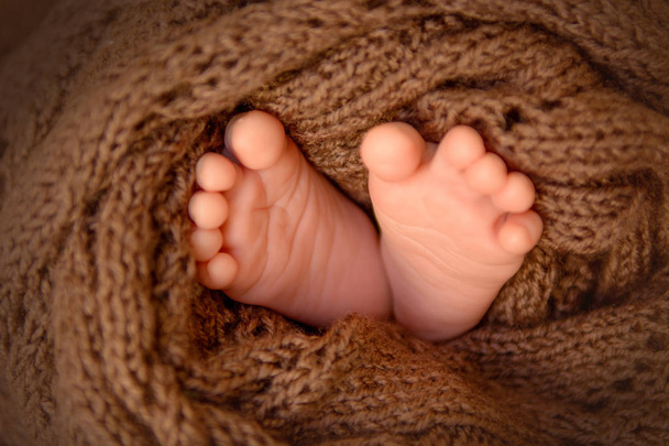 Όμορφη μικρή τακούνια από ένα νεογέννητο μωρό τυλιγμένο σε ένα κομμάτι καφέ πλεκτό ύφασμα - Φωτογραφία, εικόνα