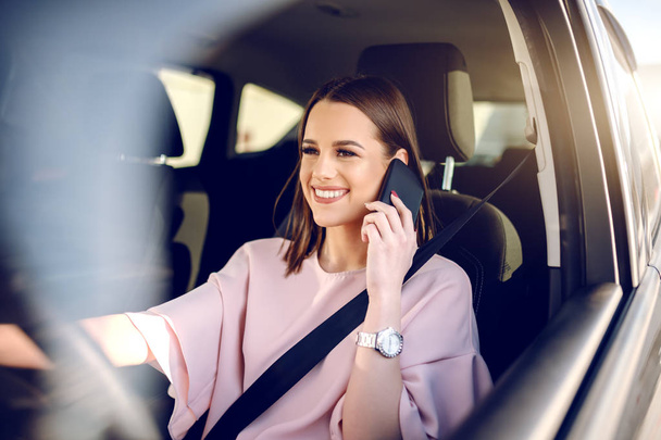 Portrait of gorgeous brunette with big toothy smile driving car and using smart phone. - Fotoğraf, Görsel