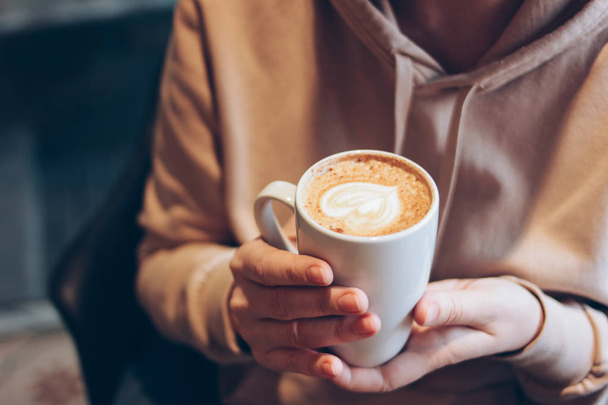Šálek kávy cappuccino s pěnovým srdcem ve ženské ruce v kavárně zblízka - Fotografie, Obrázek