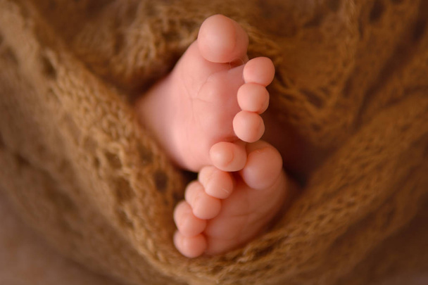 Mooie kleine hakken van een pasgeboren baby in een bruin gebreide stuk doek gewikkeld - Foto, afbeelding