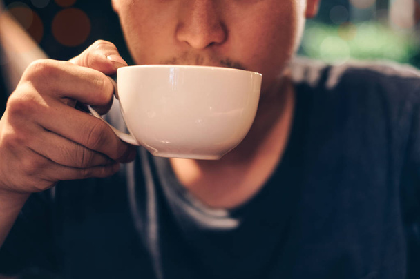 Junger Mann nimmt Schluck aus Kaffeetasse in Café - Foto, Bild