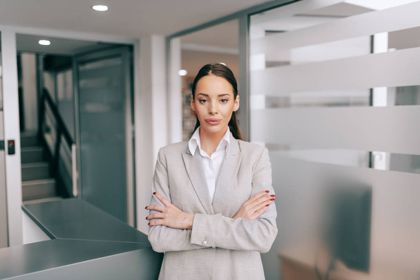 Charming Caucasian businesswoman in formal wear standing in office with arms crossed. Successful entrepreneurs are givers, not takers of positive energy. - Photo, image